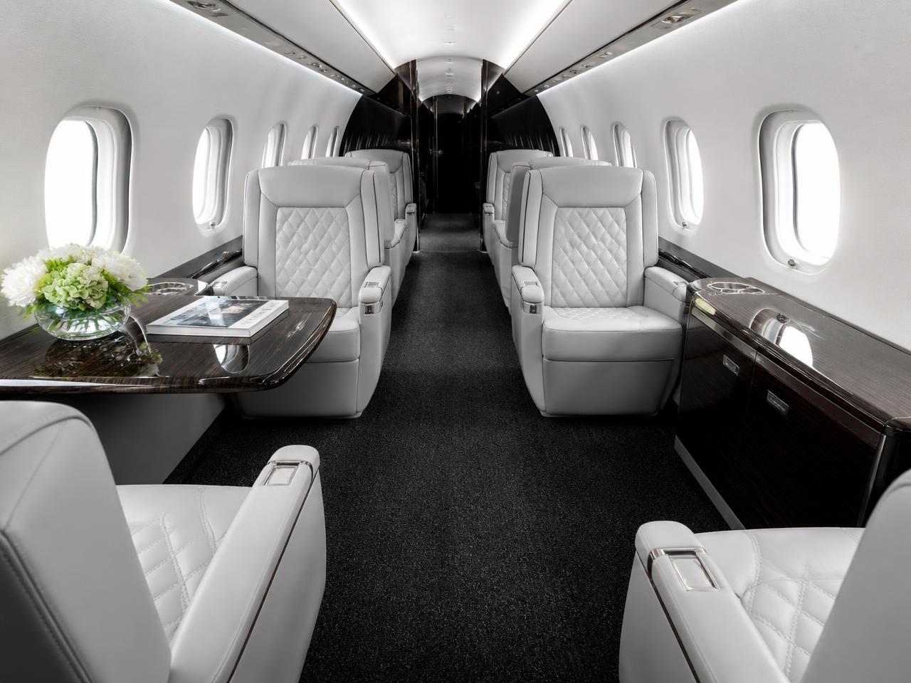 Detailed private jet cabin with white and grey quilted leather seats and dark veneer tables